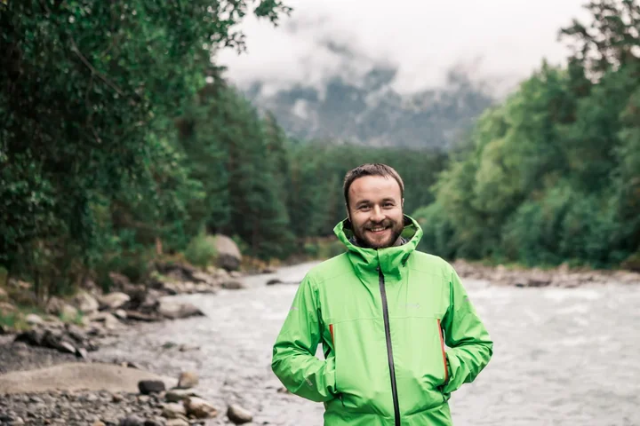 Zdjęcie przedstawia mężczyzne w zielonej kurtce przeciwdeszczowej