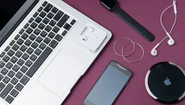 Laptop, smartfon, smartwatch i słuchawki na fioletowym blacie.
