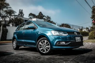 Niebieski Volkswagen typu hatchback zaparkowany na podjeździe, widok z przodu z lewej strony.