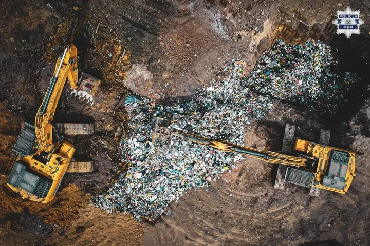 Dwa żółte koparki pracują na wysypisku śmieci, przerzucając stosy odpadów.